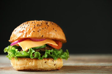 Tasty burger on wooden table against dark background