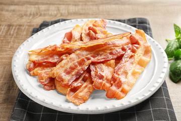 Plate with cooked bacon rashers on table