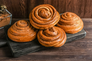 Wooden board with tasty cinnamon buns on table