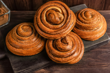 Wooden board with tasty cinnamon buns on table