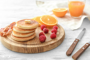 Tasty breakfast with pancakes, bacon and fruits on wooden board