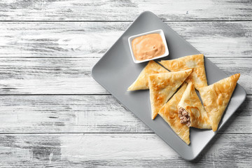 Plate with delicious meat samosas and sauce on wooden background
