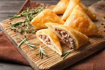 Wooden board with delicious meat samosas on table