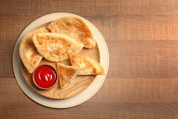 Wooden plate with delicious meat samosas and sauce on table