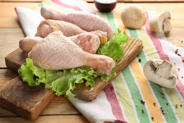 Wooden board with raw chicken legs and lettuce on table