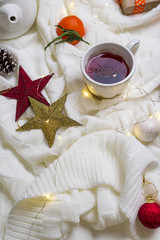 Hot Cup of tea with tangerines and sweaters on bed