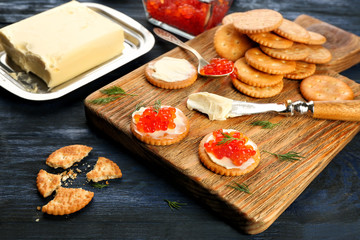 Crackers with butter and red caviar on wooden board