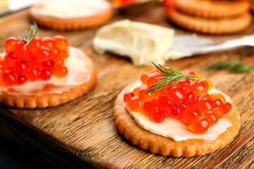 Cracker with butter and red caviar on wooden board, closeup