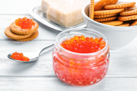 Glass jar and spoon with red caviar on table