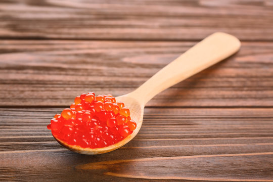 Spoon with delicious red caviar on wooden background