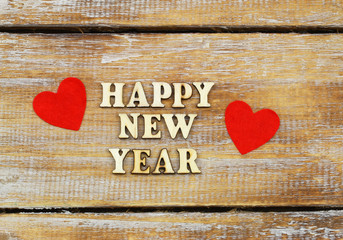 Happy New Year written with wooden letters on rustic surface and two red hearts
