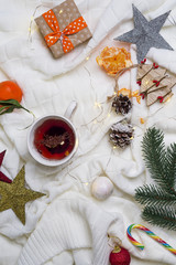 Cup of tea with tangerines and sweaters on bed background