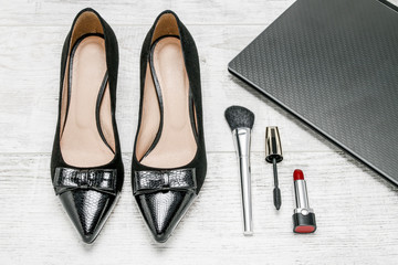 Black shoes, notebook and cosmetics on wooden floor.
