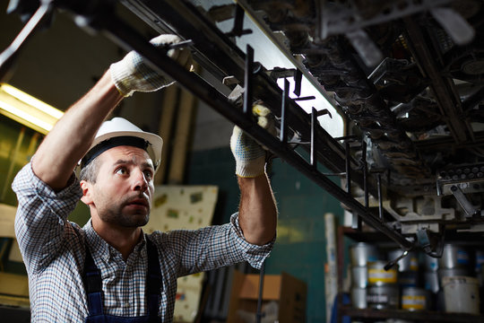 Mid-aged worker in hardhat and uniform repairing ar carrying out technical revision of machine