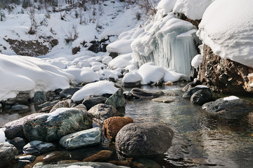 Winter landscape of mountain river with stones and small frozen waterfall