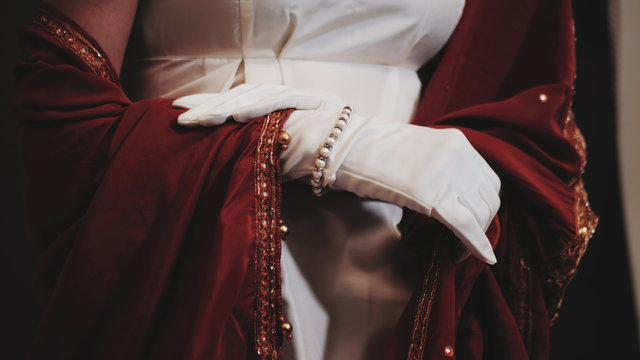 Luxurious retro woman with expensive jewelry in white and red historical 18th century dress posing. Girl in long silk gloves.
