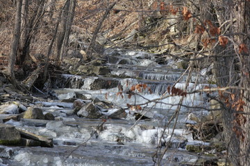 Cascading water down a slight hilly and rocky incline. Ice beginning to form on rocks at the...
