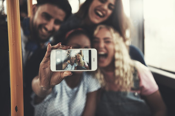 Smiling friends taking selfies with a smartphone on the bus