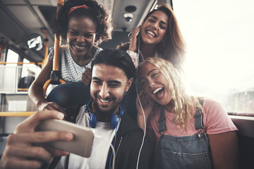 Smiling friends sitting on a bus listening to music together