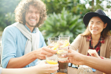 Hands of friendly people with glasses of refreshing homemade lemonade toasting by dinner