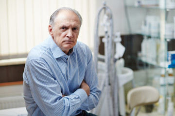 Sick old man with arms crossed on chest waiting for doctor in hospital