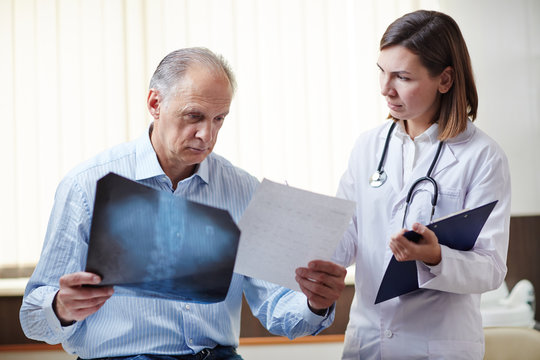 Young doctor showing x-ray image to sick retired patient and giving him recommendations about medical treatment