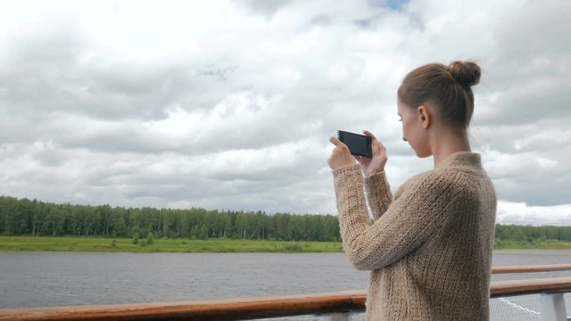 Woman taking photo of landscape with smartphone on deck of cruise ship. Photography, nature and journey concept