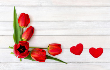 Beautiful red tulips and two hearts on background of white painted wooden planks with space for text. Top view, flat lay. Valentine decoration.