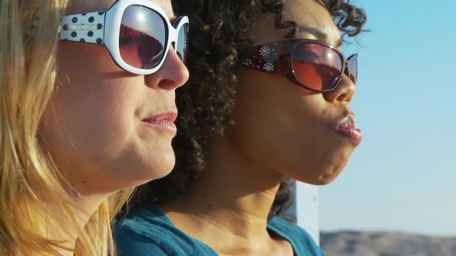 Two women friends in sunglasses blowing bubblegum at the beach