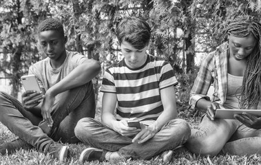 Group of multi ethnic teenagers using tablets and smartphones seated on the grass