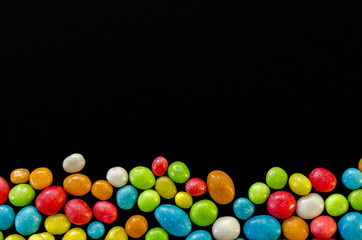 Multicolored candy on black background with space for text