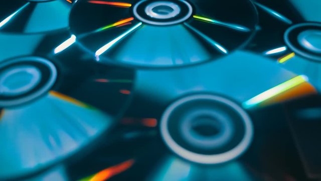 Many compact discs lying on top of each other rotate and shimmer in different colors. Macro. Closeup. Shallow depth of field. Jib arm
