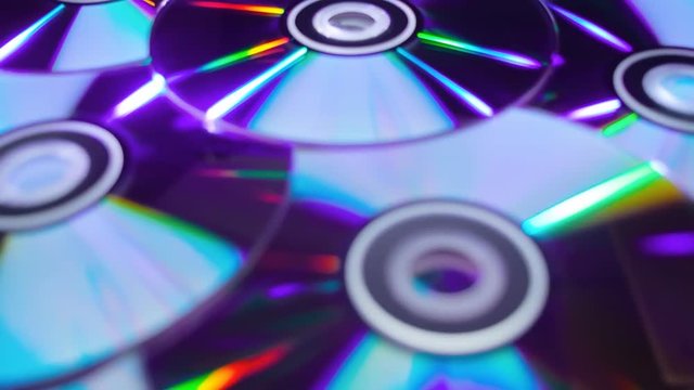 Many compact discs lying on top of each other rotate and shimmer in different colors. Macro. Closeup. Shallow depth of field. Jib arm
