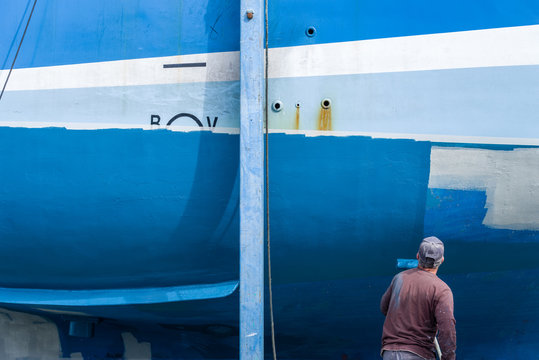 Un homme peint la coque d&rsquo;un bateau