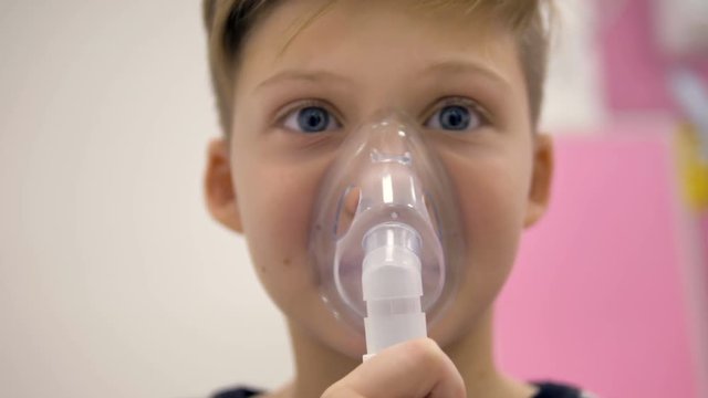 A close-up on a boys face hidden by an inhaler mask. 