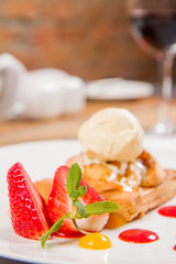 Apple pie with ice-cream decorated with a strawberry, fruit sauce and herb served in a restaurant