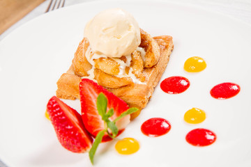 Apple pie with ice-cream decorated with a strawberry, fruit sauce and herb served in a restaurant