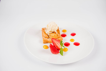 Apple pie with ice-cream decorated with a strawberry, fruit sauce and herb on a white background