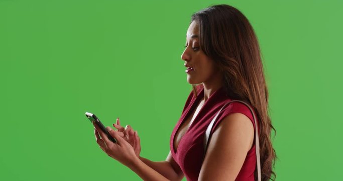 Profile of beautiful Latina female messaging on smart phone on green screen. On green screen to be keyed or composited. 