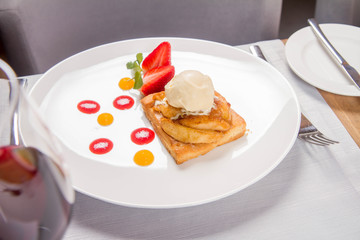 Apple pie with ice-cream decorated with a strawberry, fruit sauce and herb served in a restaurant