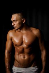 Fototapeta na wymiar Shirtless muscular and tanned bodybuilder guy on the black background
