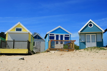 Fototapeta na wymiar Three English seaside beach huts for summer travel destination. Warm blue sky background.