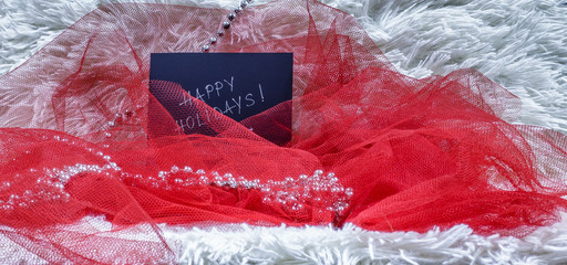 Happy holidays text on black card with red tulle and beads on white fluffy background