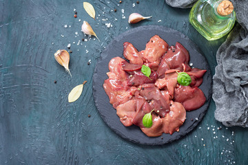 Raw chicken liver on a slate board and spices on a stone with a gray stone background. Top view.