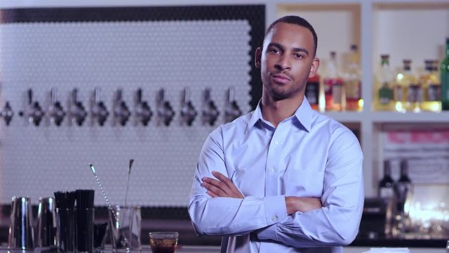 Portrait shot of a young attractive African American man smiling with his arms crossed at a bar