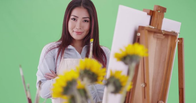 A young asian woman paints near sunflowers on green screen. On green screen to be keyed or composited. 