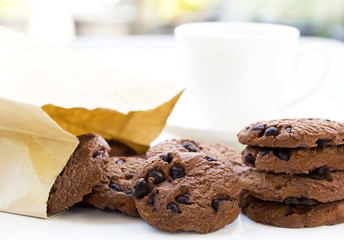 Traditional chocolate chip cookies and paper bag with cup coffee on table white with home garden background. With copy space for text.