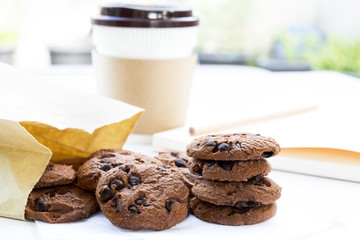 Traditional chocolate chip cookies and paper bag with cup coffee on table white with home garden background. With copy space for text.