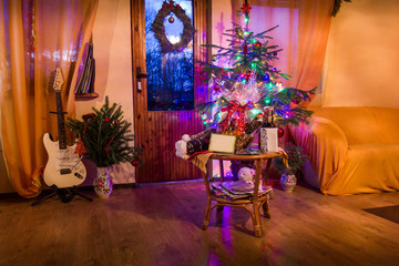 Fototapeta na wymiar A living room lighted with numerous lights decorated ready to celebrate Christmas. Christmas tree decorated by lights and garland lighting indoors fireplace.