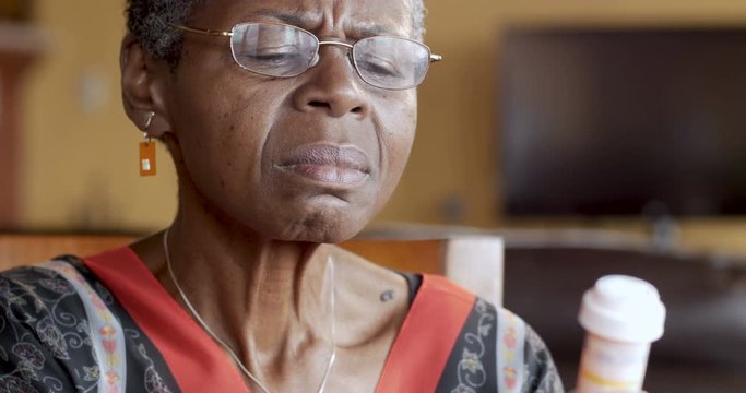 Black senior woman putting on glasses to read her prescription bottle